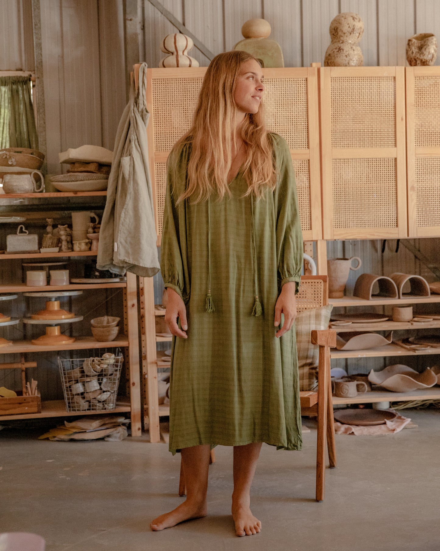 
                  
                    woman dressed in flores organic sugarcane dress in forest green standing in pottery studio with ceramics in background
                  
                