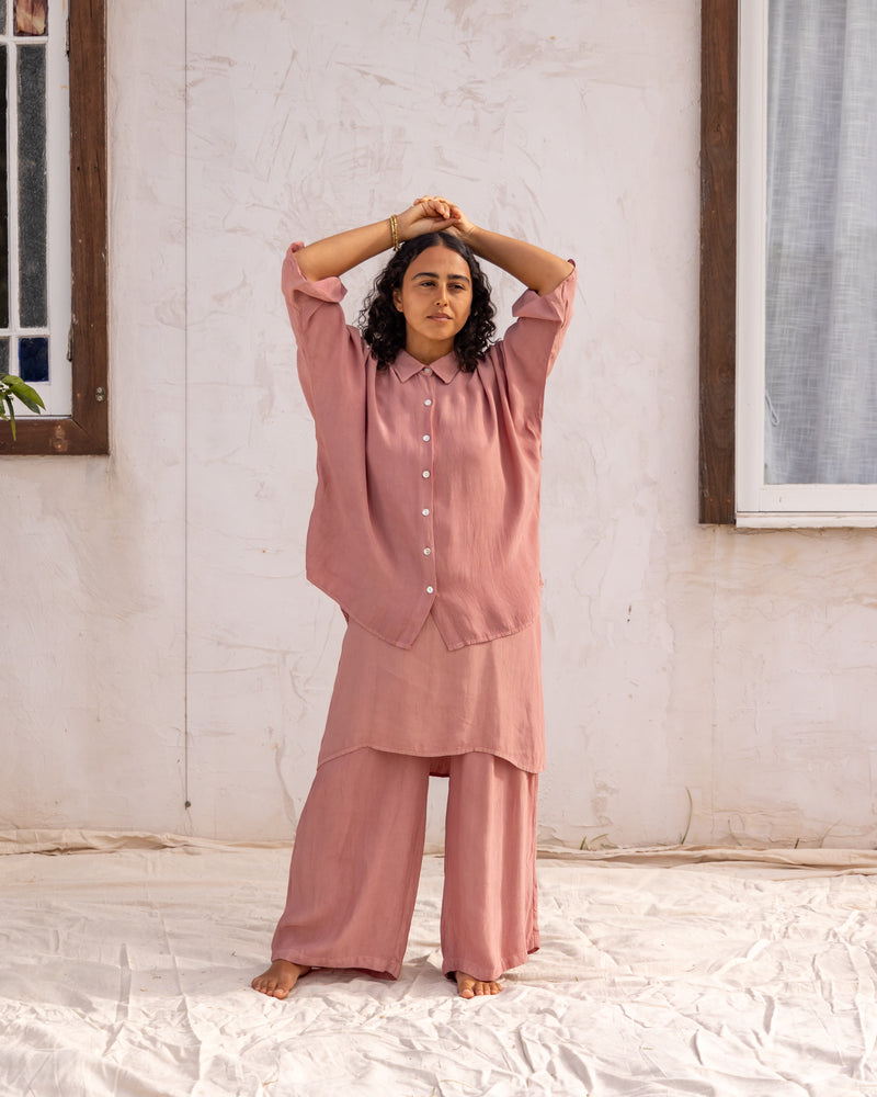 
                  
                    woman dressed in bouviet oversized shirt and miguel straight legged pants in orange peel fibre in dirty rose pink standing in front of a white wall
                  
                