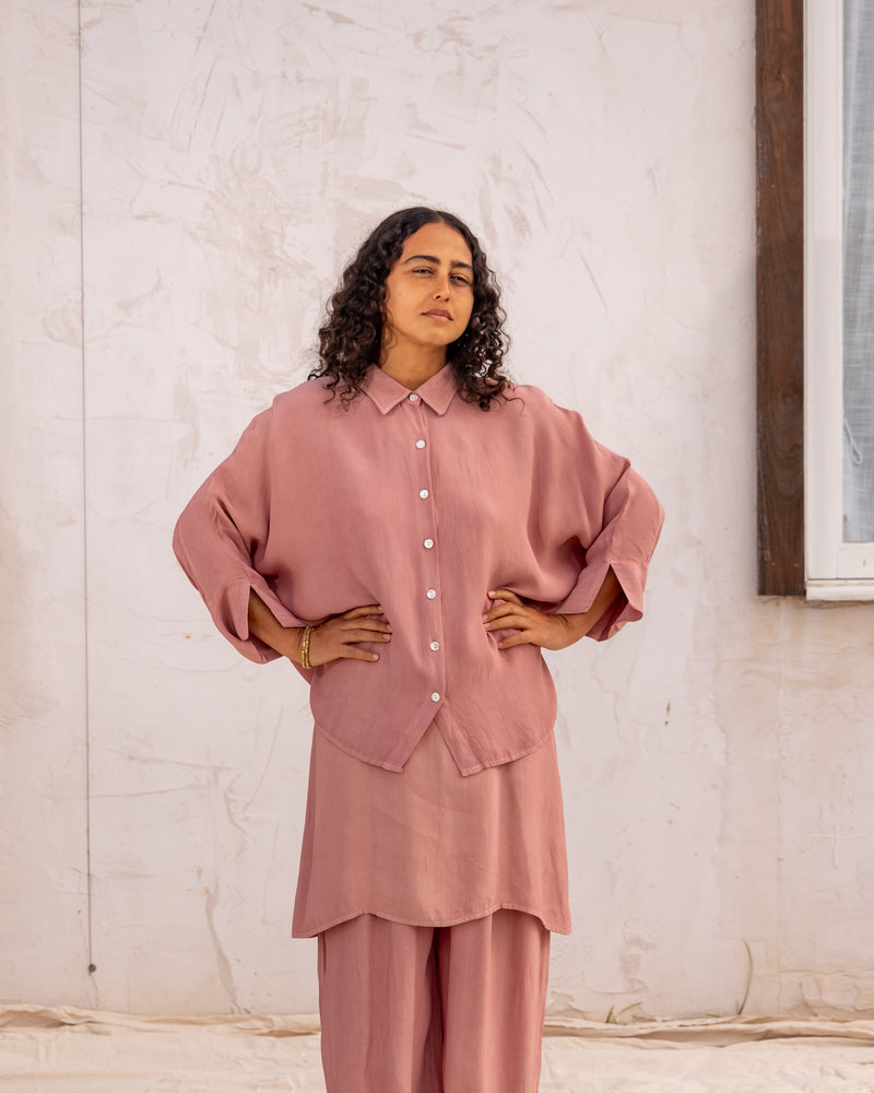 
                  
                    woman dressed in bouviet oversized shirt and miguel straight legged pants in orange peel fibre in dirty rose pink standing in front of a white wall
                  
                