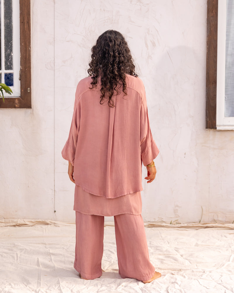 
                  
                    woman dressed in bouviet oversized shirt and miguel straight legged pants in orange peel fibre in dirty rose pink standing in front of a white wall
                  
                