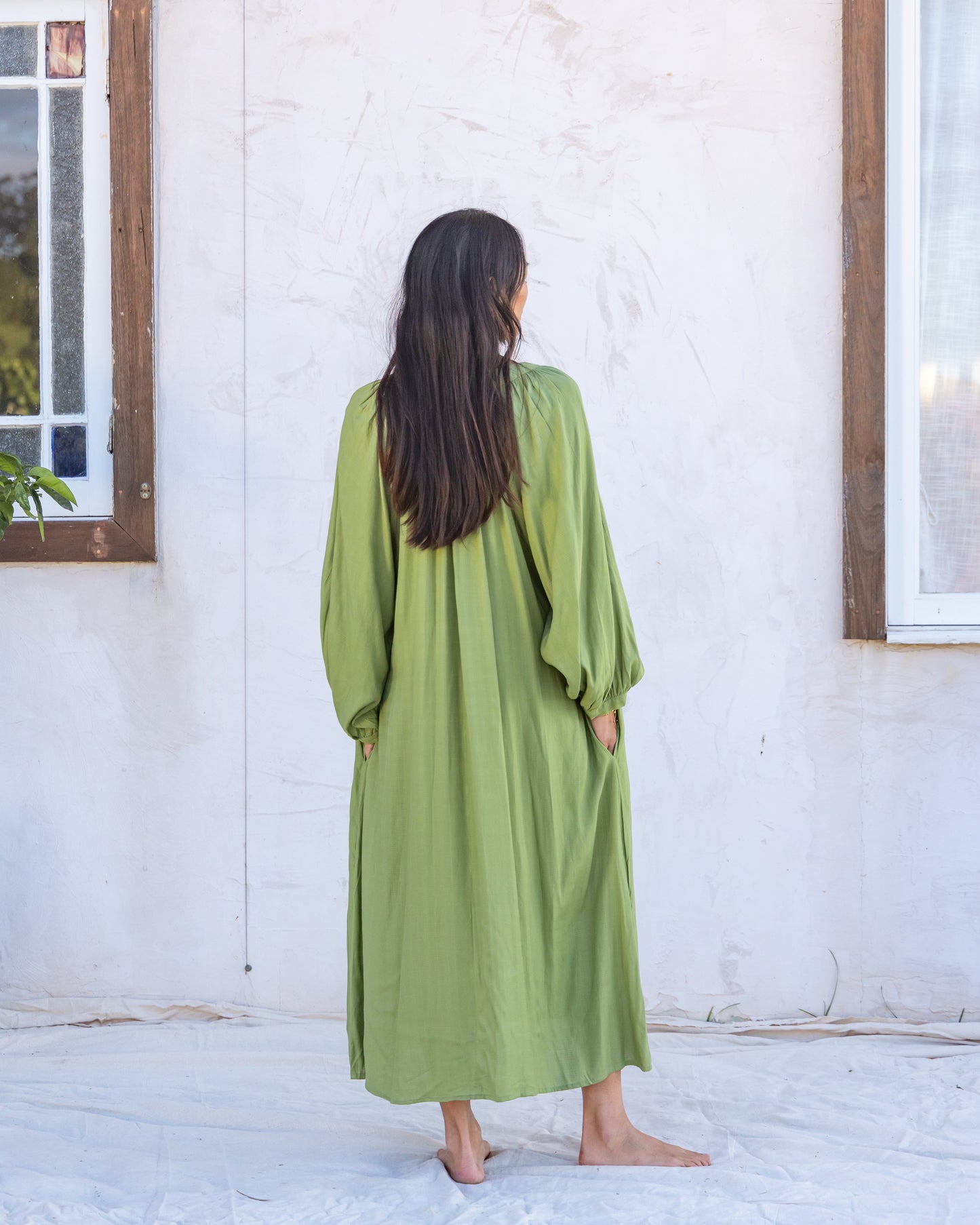 woman dressed in flores organic sugarcane dress in forest green in front of white wall