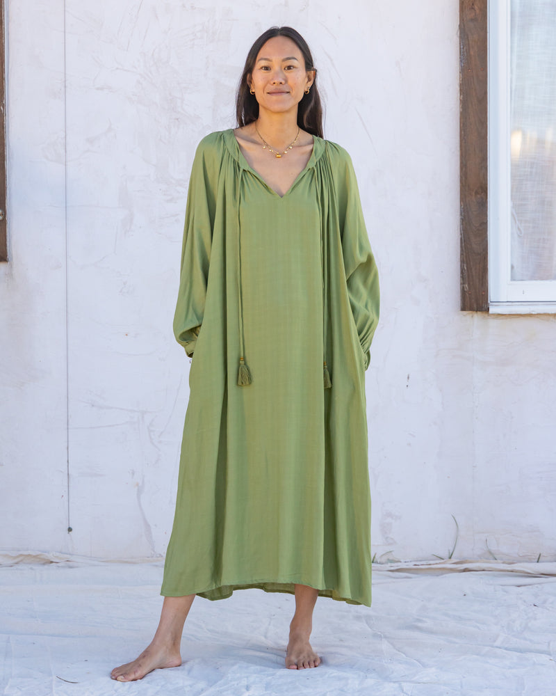 woman dressed in flores organic sugarcane dress in forest green in front of white wall
