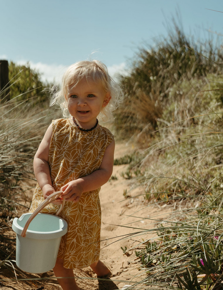 
                  
                    Young girl with bucket on beach in fogo straight dress in mustard seed print
                  
                