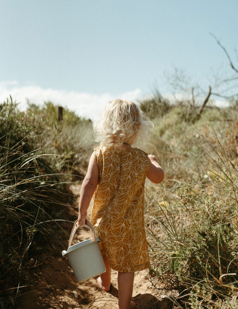 
                  
                     Young girl with bucket on beach in fogo straight dress in mustard seed print
                  
                