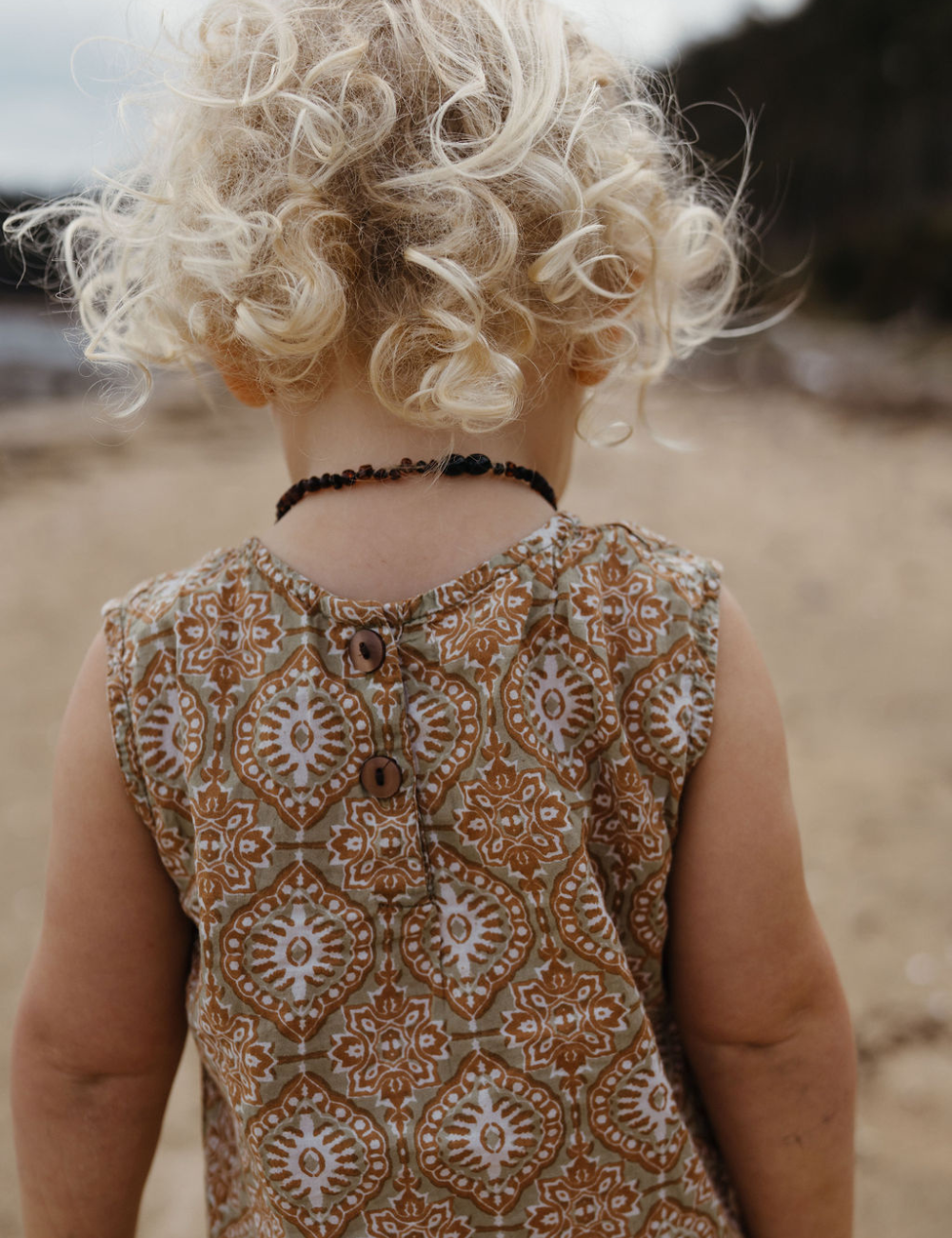 
                  
                    back of girl with curly hair on beach in fogo straight dress in retro funk print
                  
                
