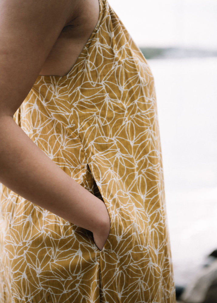 
                  
                    woman dressed in mustard and white patterned midi dress in front of ocean
                  
                