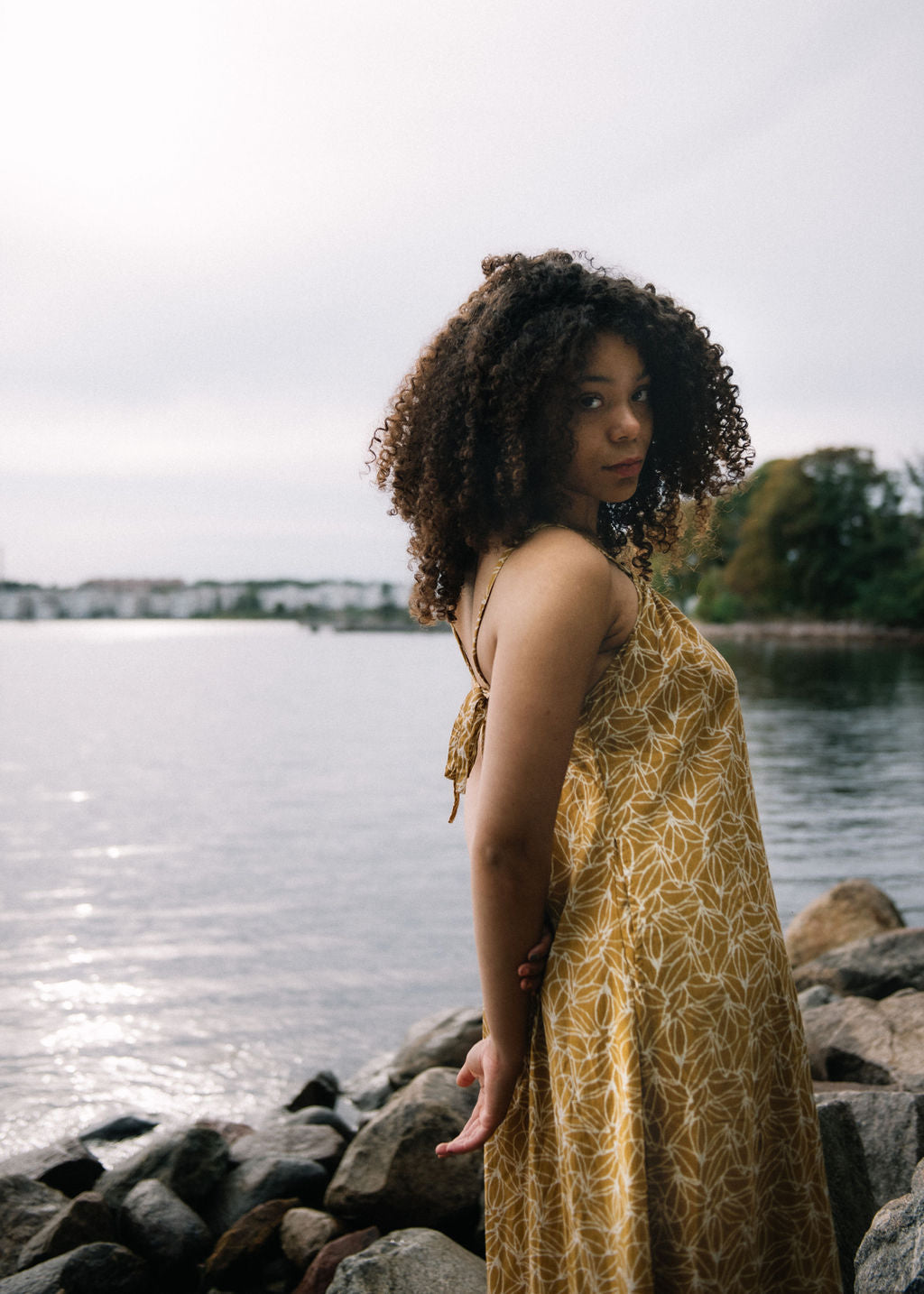 
                  
                    woman dressed in mustard and white patterned midi dress on rocky beach in front of ocean
                  
                