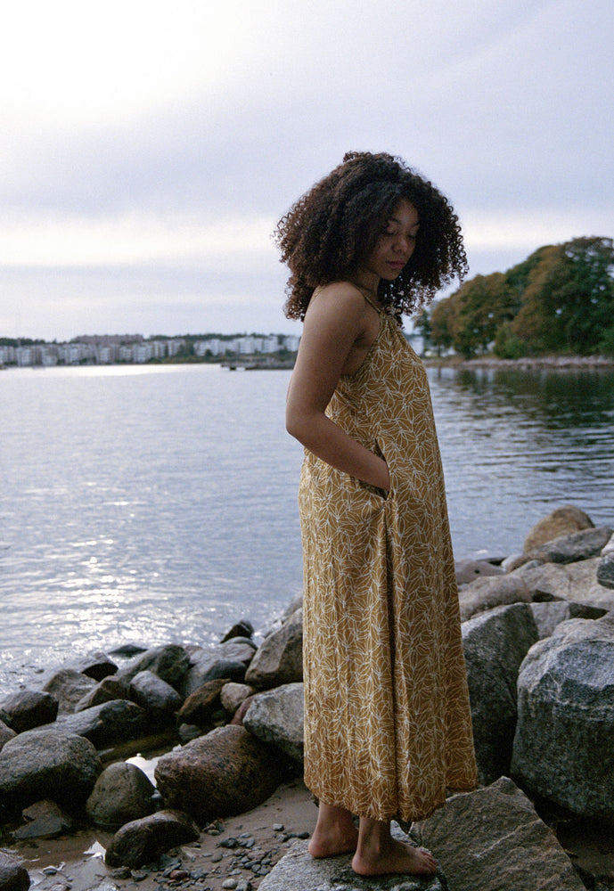 
                  
                    woman dressed in mustard and white patterned midi dress in front of ocean
                  
                