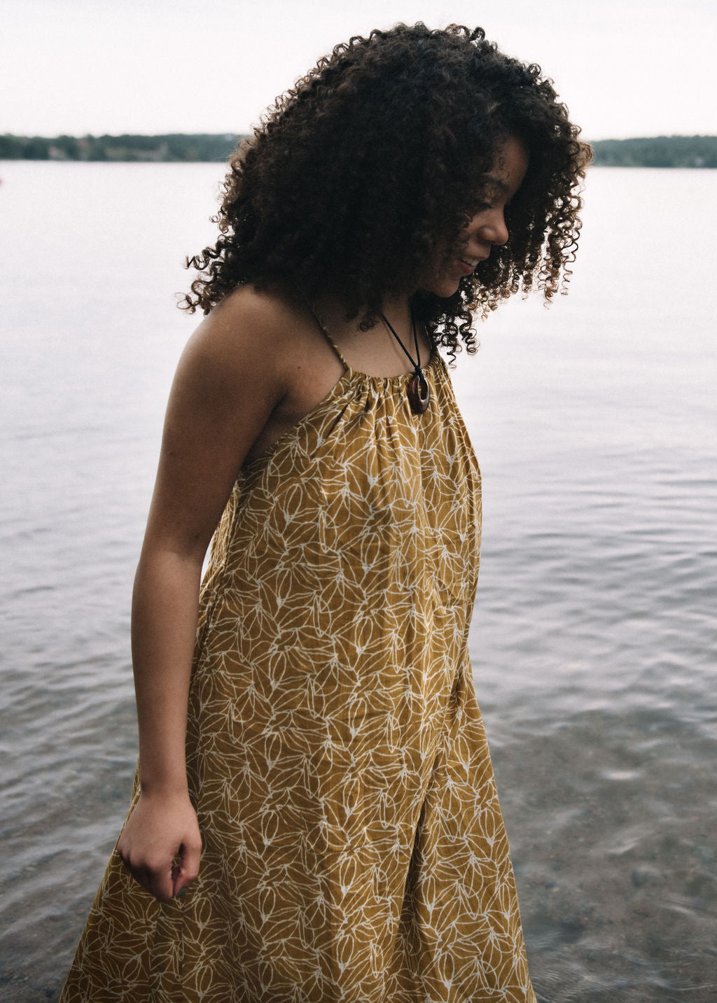 
                  
                    woman dressed in mustard and white patterned midi dress in front of ocean
                  
                