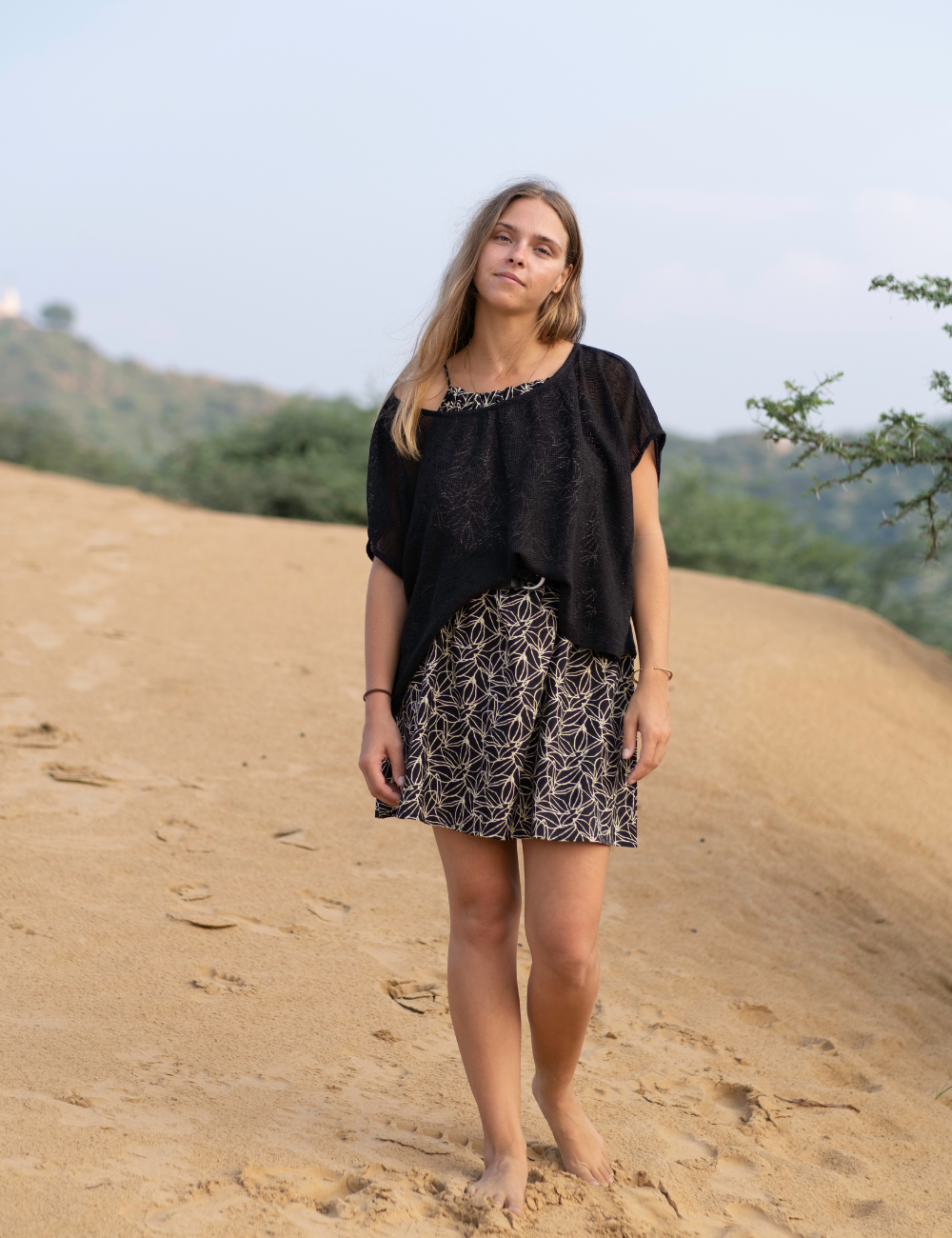woman dressed in dark patterned mini dress with oversized net charcoal top in Indian desert