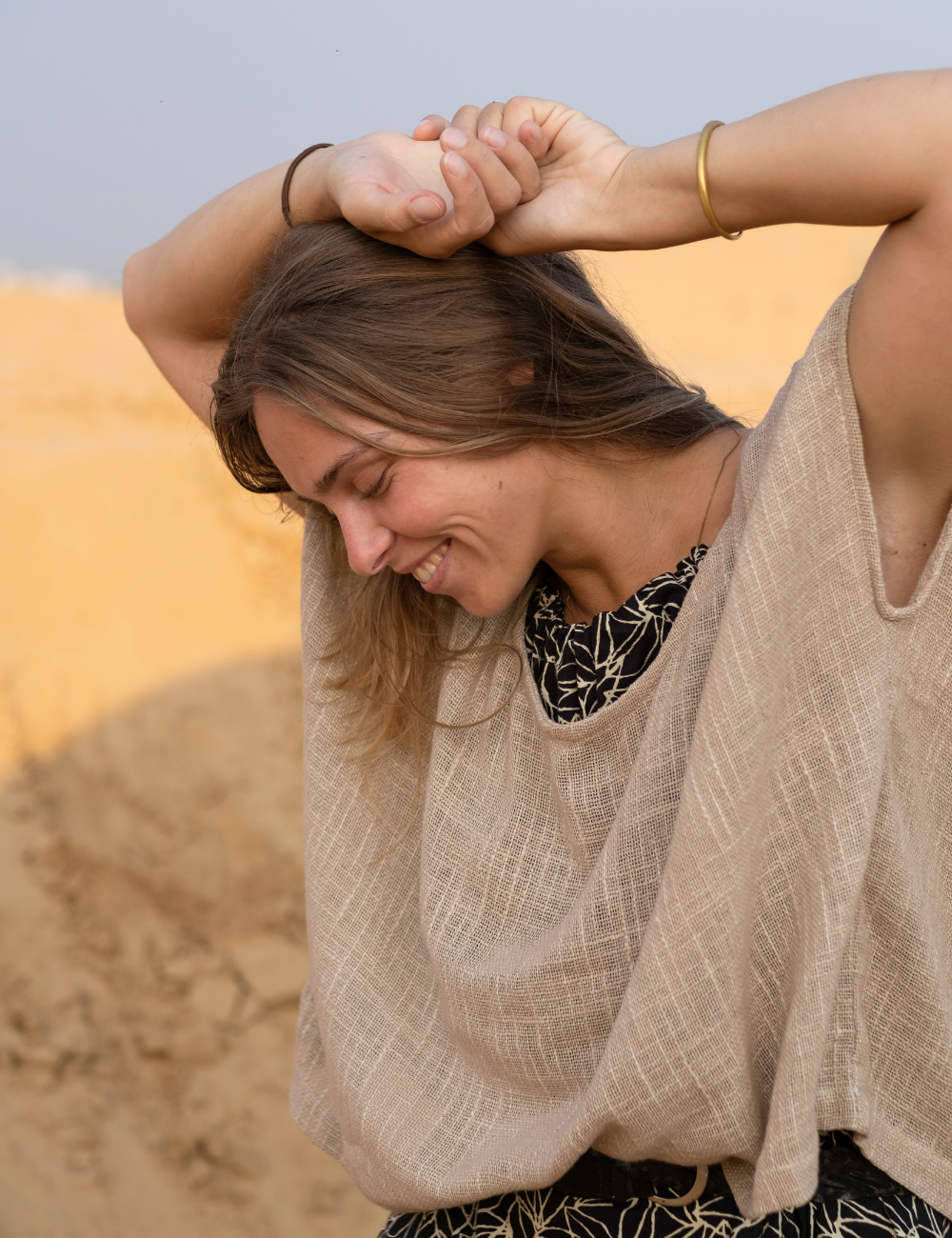 
                  
                    woman laughing dressed in dark patterned mini dress with oversized taupe coloured top in Indian desert
                  
                