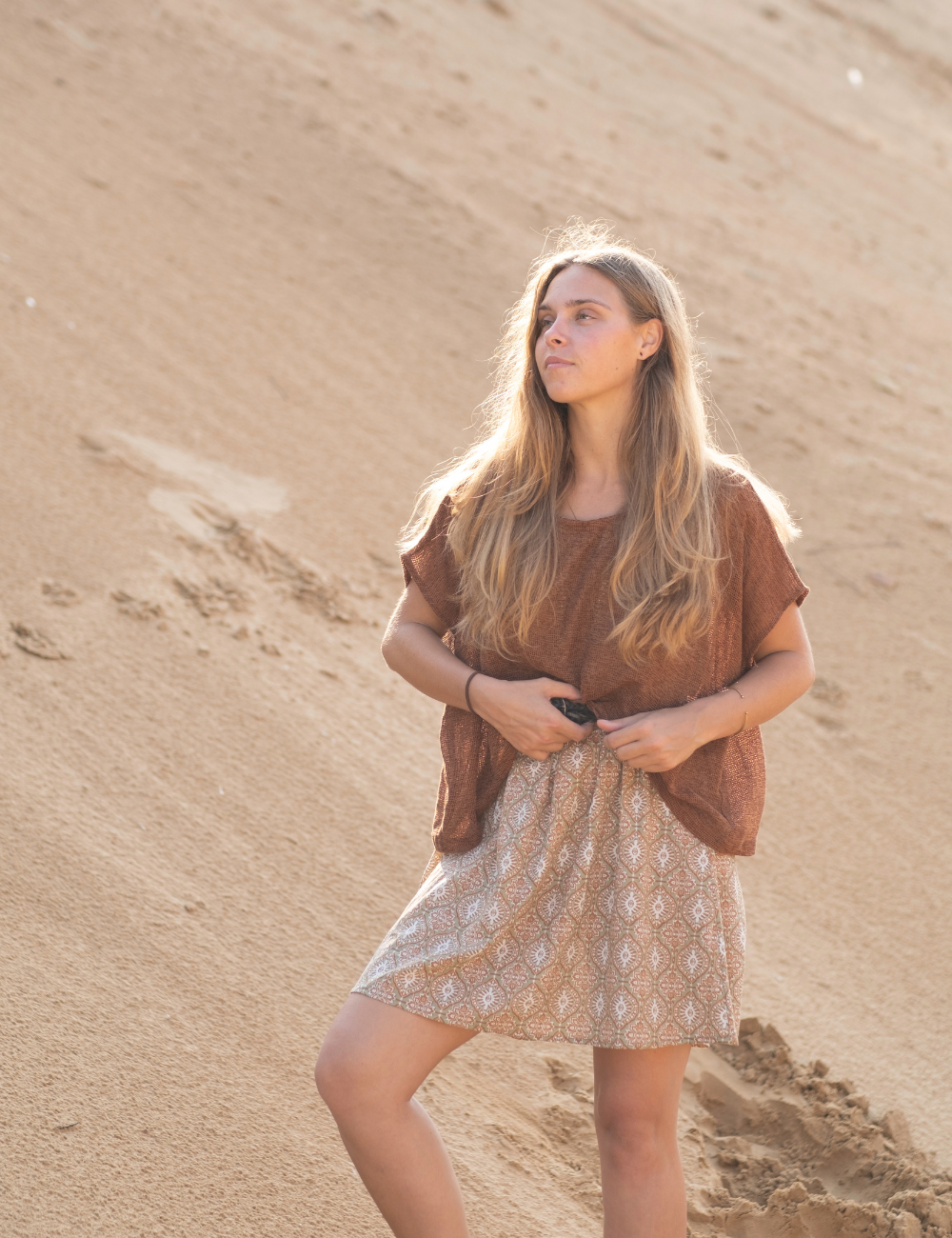 
                  
                    woman dressed in light coloured retro patterned mini dress with oversized net rust top in Indian desert
                  
                