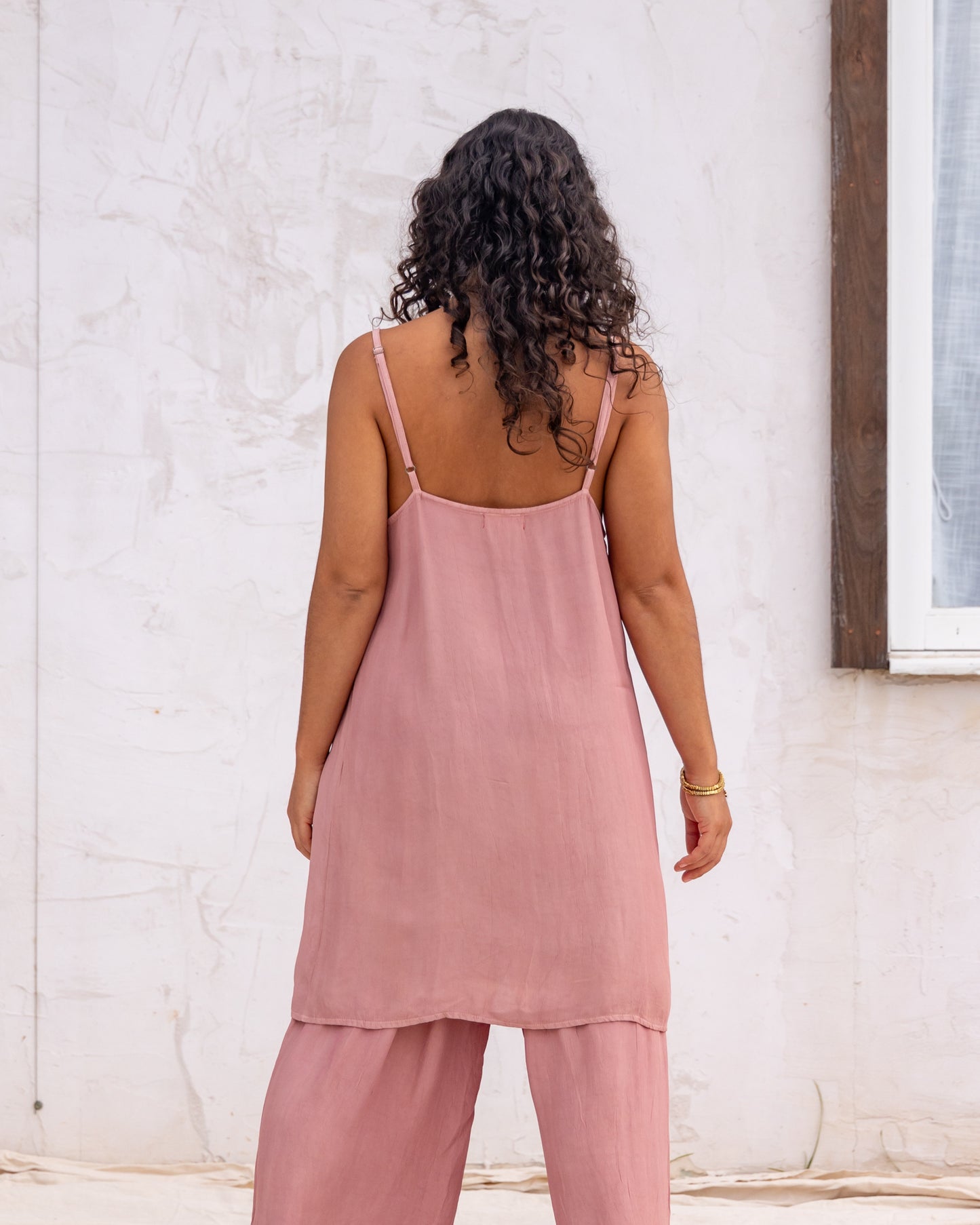 
                  
                    woman dressed in miguel straight legged pants and maio mini slip in orange peel fibre in dirty rose pink standing in front of a white wall
                  
                