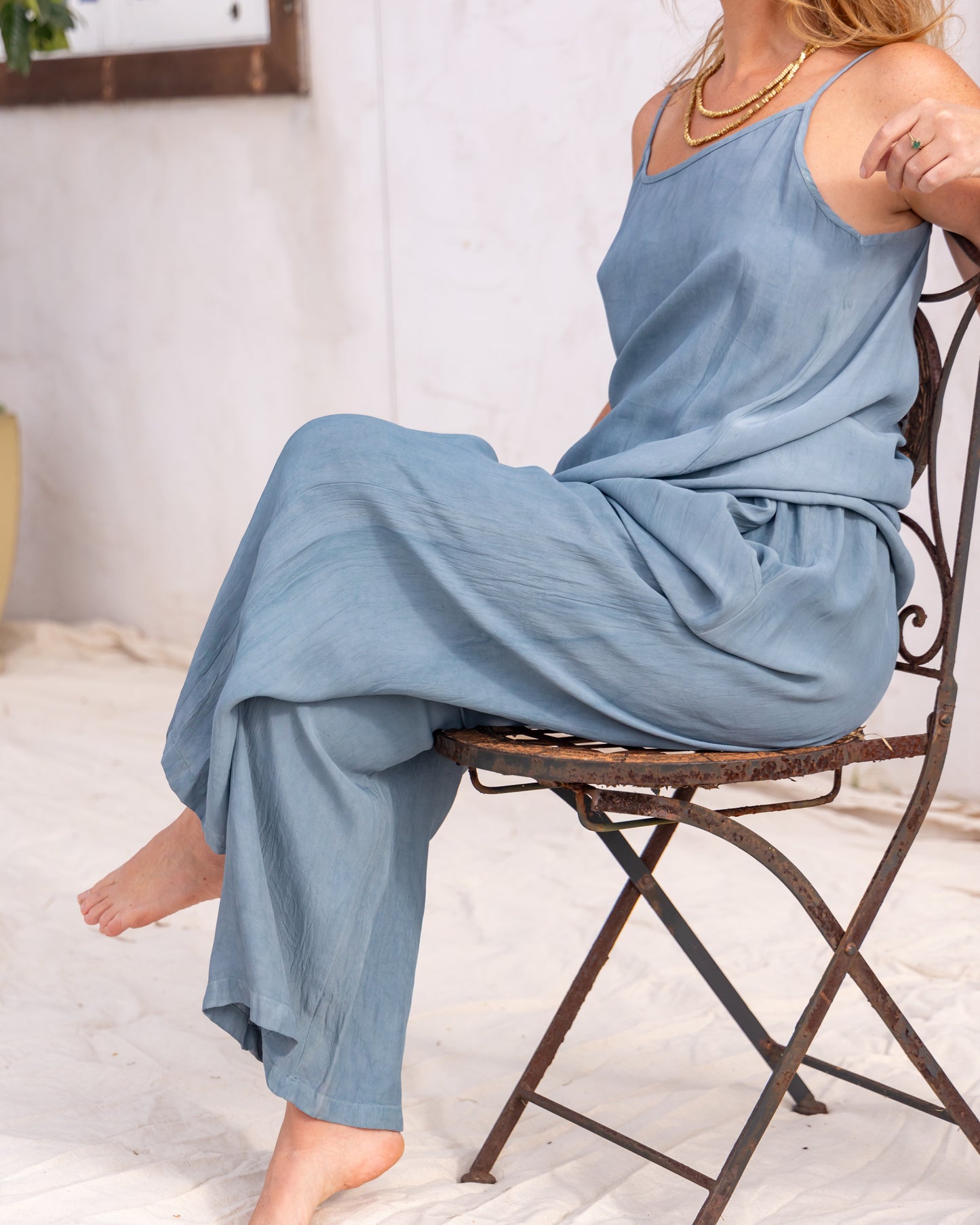 
                  
                    woman dressed in miguel straight legged pants and maio mini slip in orange peel fibre in cornflower blue sitting on a metal chair in front of a white wall
                  
                