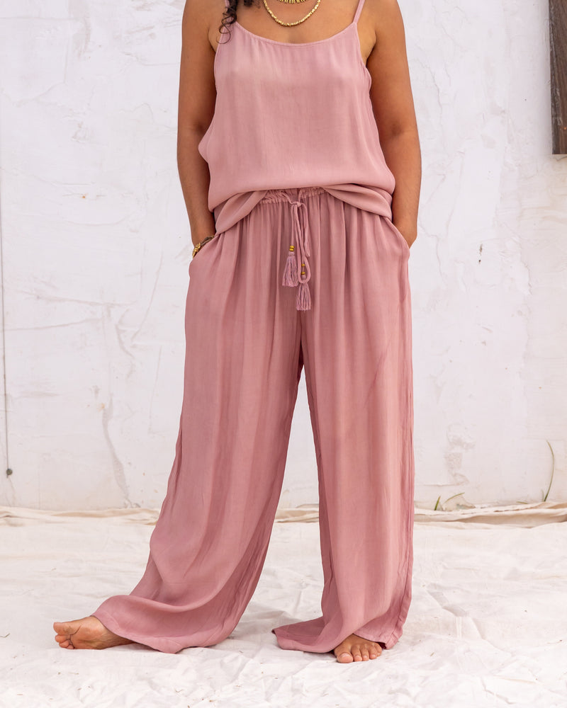 
                  
                    woman dressed in miguel straight legged pants and maio mini slip in orange peel fibre in dirty rose pink standing in front of a white wall
                  
                