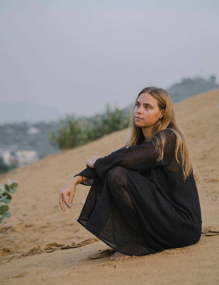 
                  
                    woman dressed in oversized maxi dress in net charcoal sitting in Indian desert with plant in background
                  
                