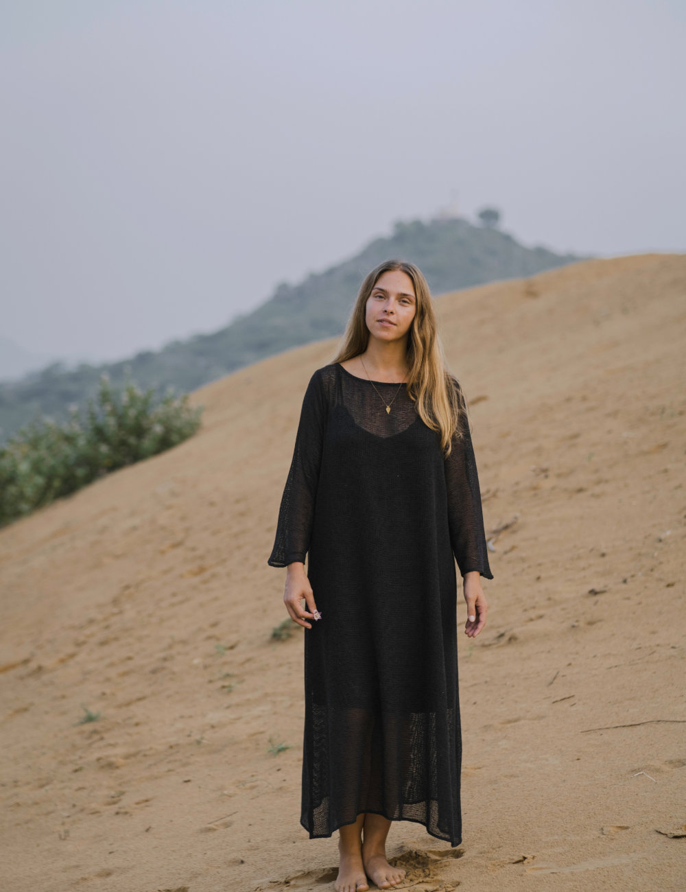 
                  
                    woman dressed in oversized maxi dress in net charcoal in Indian desert with plant in background
                  
                