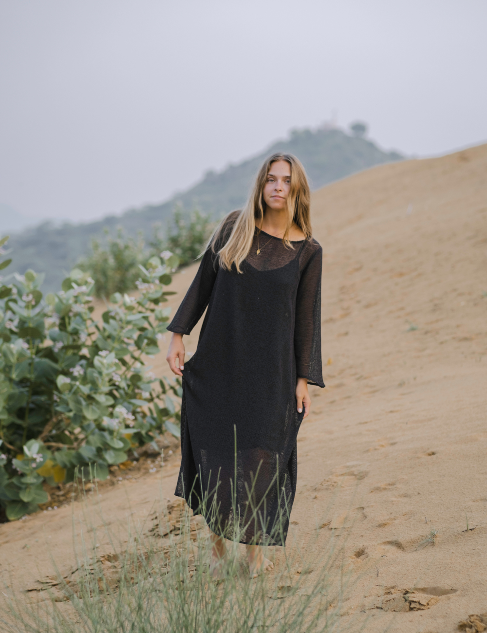 
                  
                    woman dressed in oversized maxi dress in net charcoal in Indian desert with plant in background
                  
                