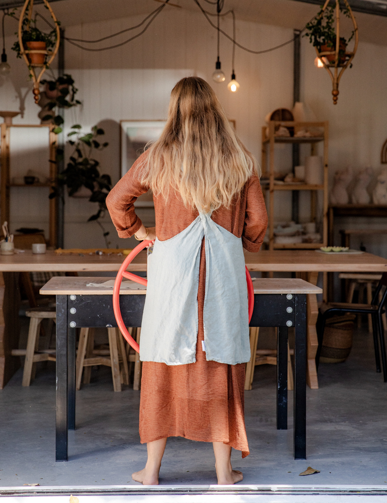 
                  
                    woman dressed in oversized maxi dress in net rust working on the slab table in pottery studio with ceramics in background
                  
                