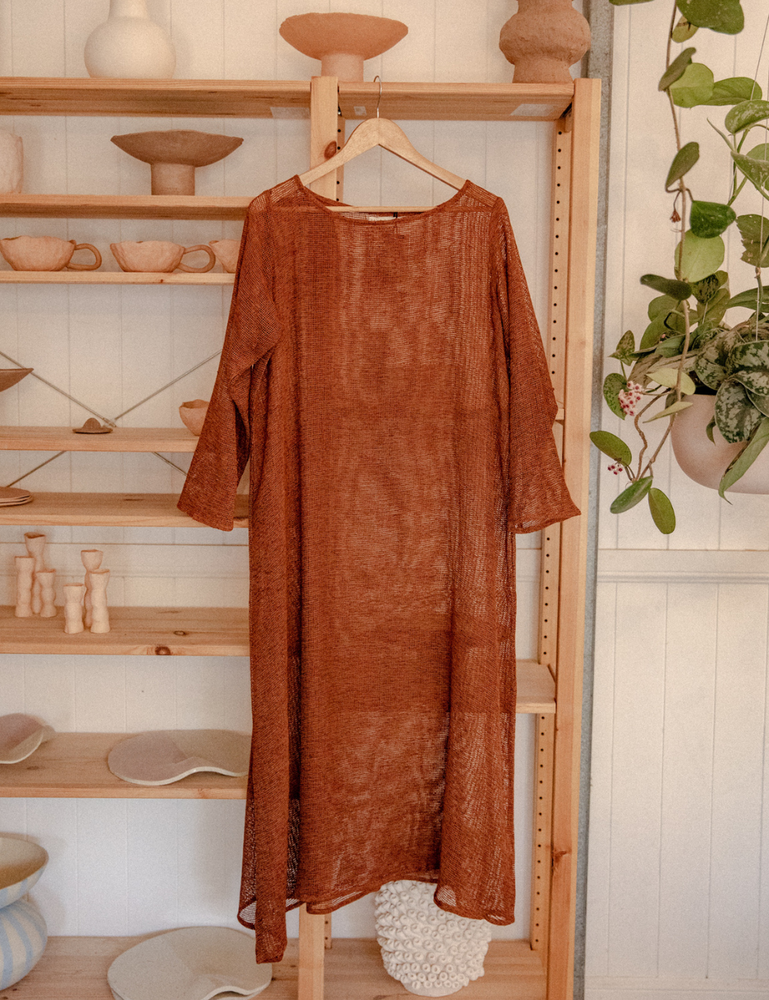 
                  
                    oversized maxi dress in net rust hanging in pottery studio with ceramics in background
                  
                