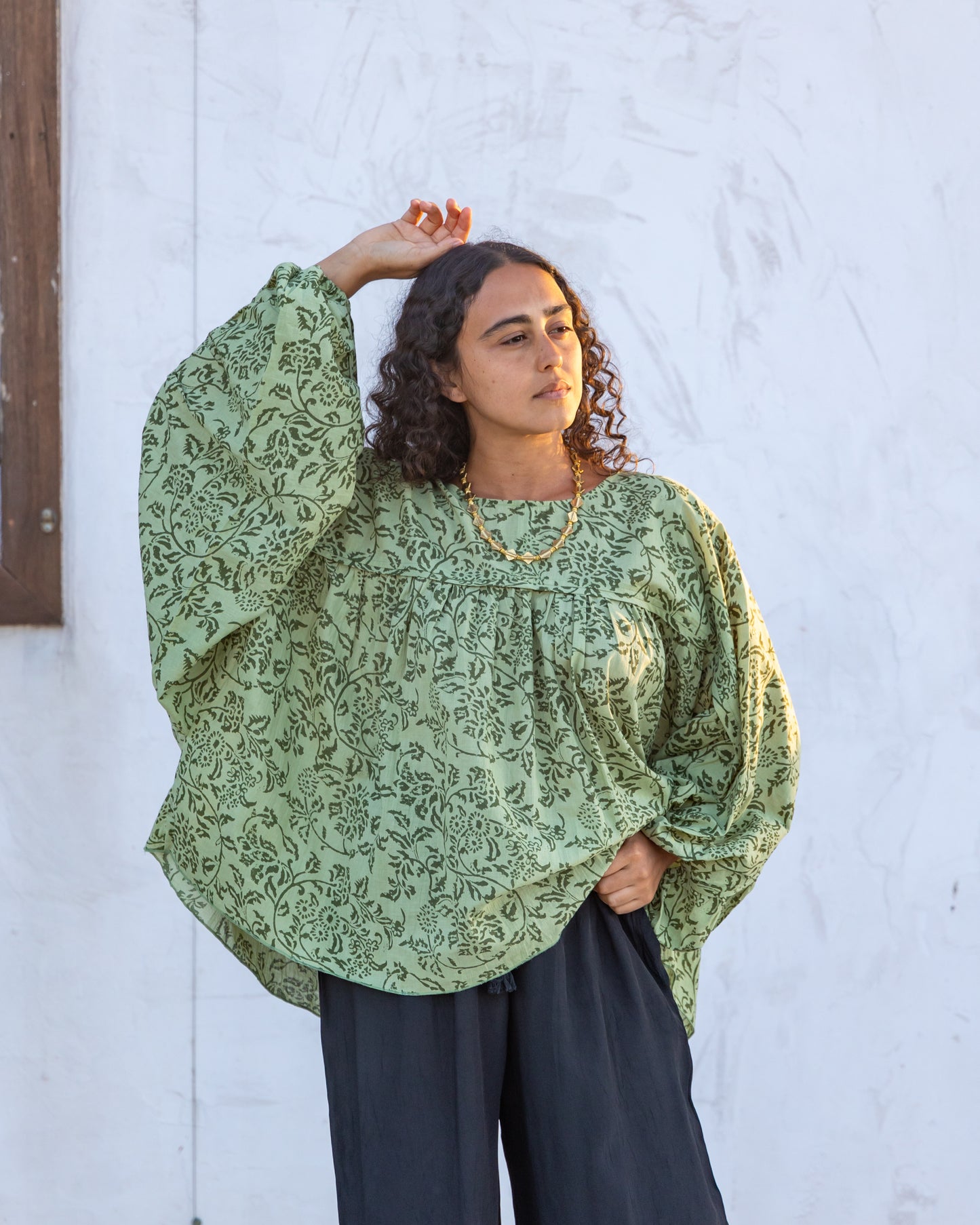 
                  
                    woman dressed in palma billowing sleeves top in gooseberry green print in front of white wall
                  
                