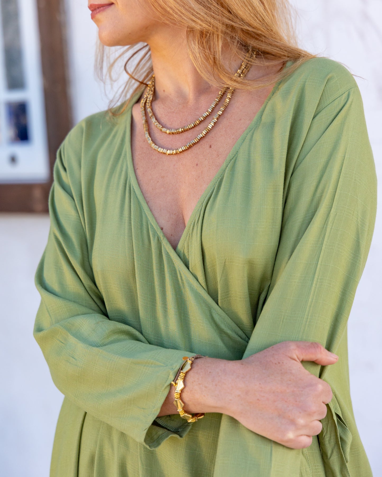 woman dressed in santo organic sugarcane wrap dress in green forest standing in front of a white wall