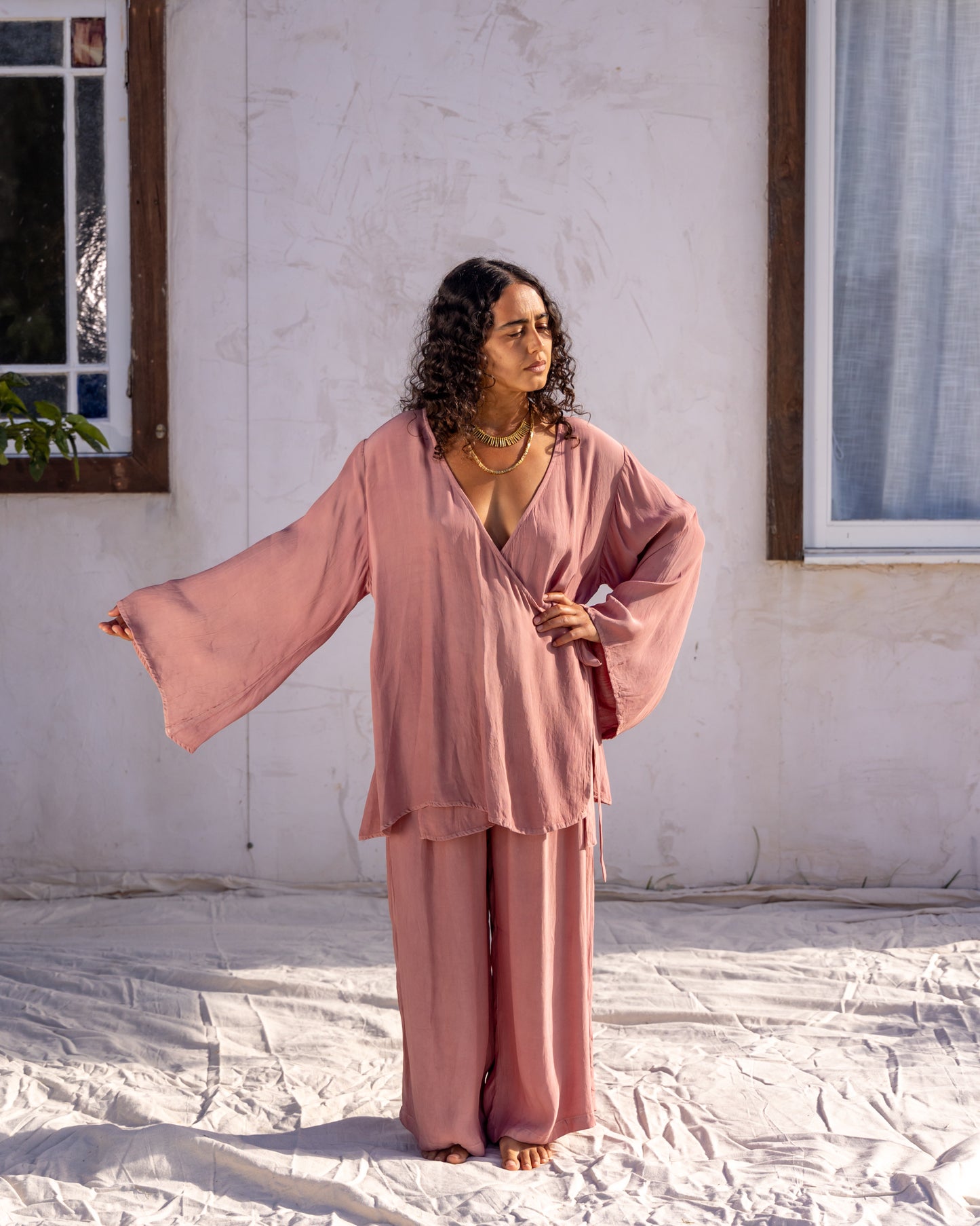
                  
                    woman dressed in sao wrap top and miguel straight legged pants in orange peel fibre in pink dirty rose standing in front of a white wall
                  
                