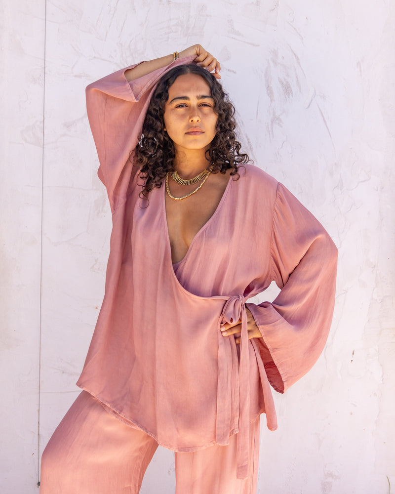 
                  
                    woman dressed in sao wrap top and miguel straight legged pants in orange peel fibre in pink dirty rose standing in front of a white wall
                  
                