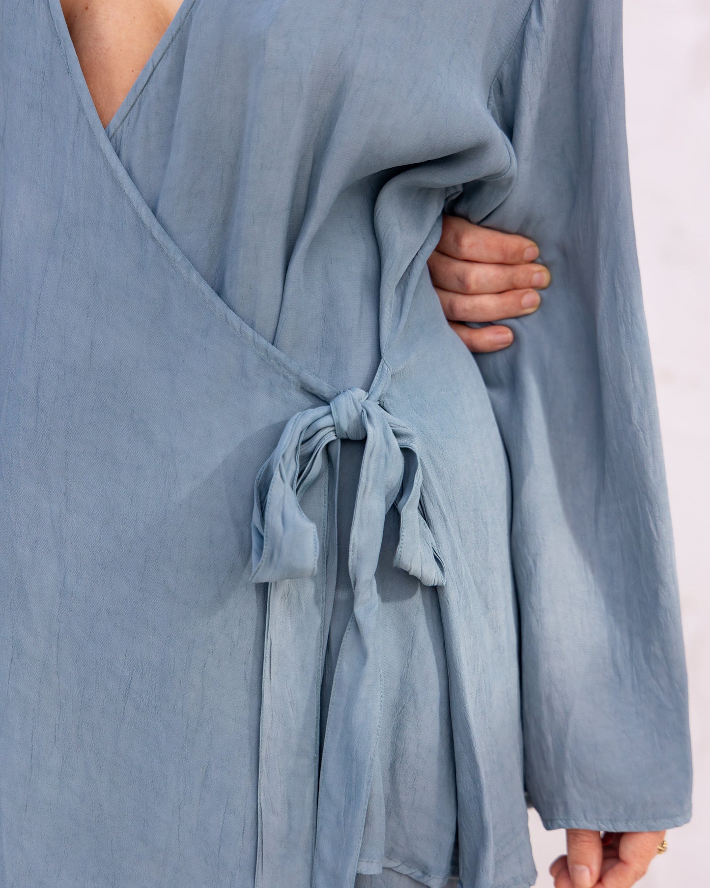 
                  
                    woman dressed in sao wrap top and miguel straight legged pants in orange peel fibre in blue cornflower standing in front of a white wall
                  
                