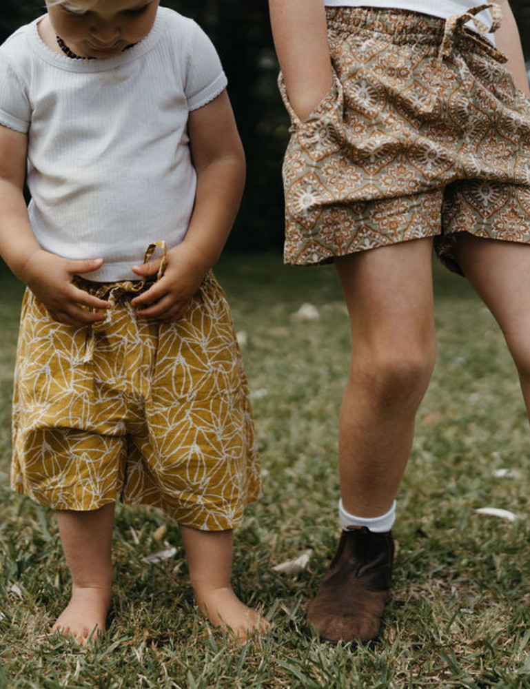 
                  
                    two young siblings wearing retro block printed shorts in mustard seed and retro funk print on lawn
                  
                