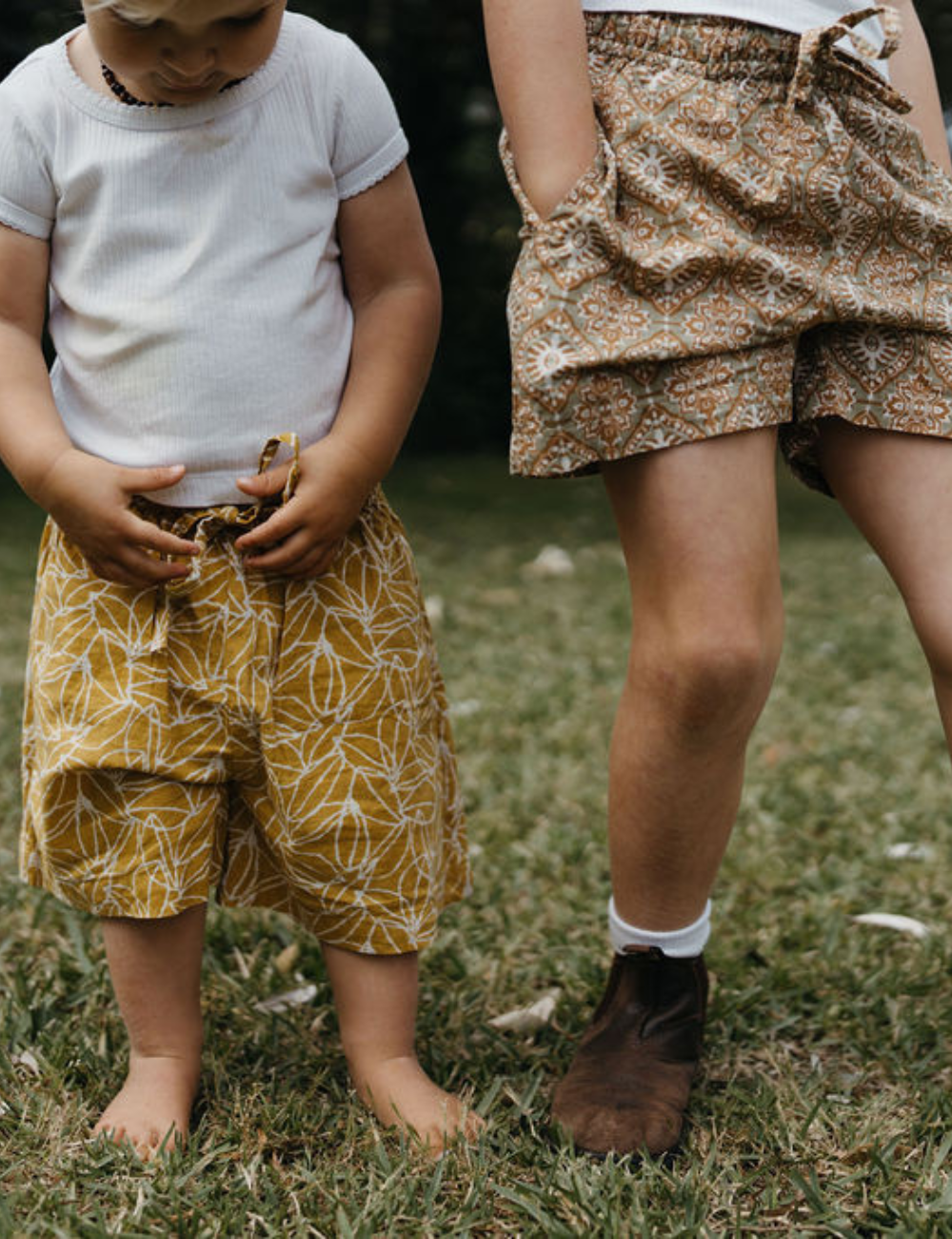 two young siblings wearing retro block printed shorts in mustard seed and retro funk print on lawn