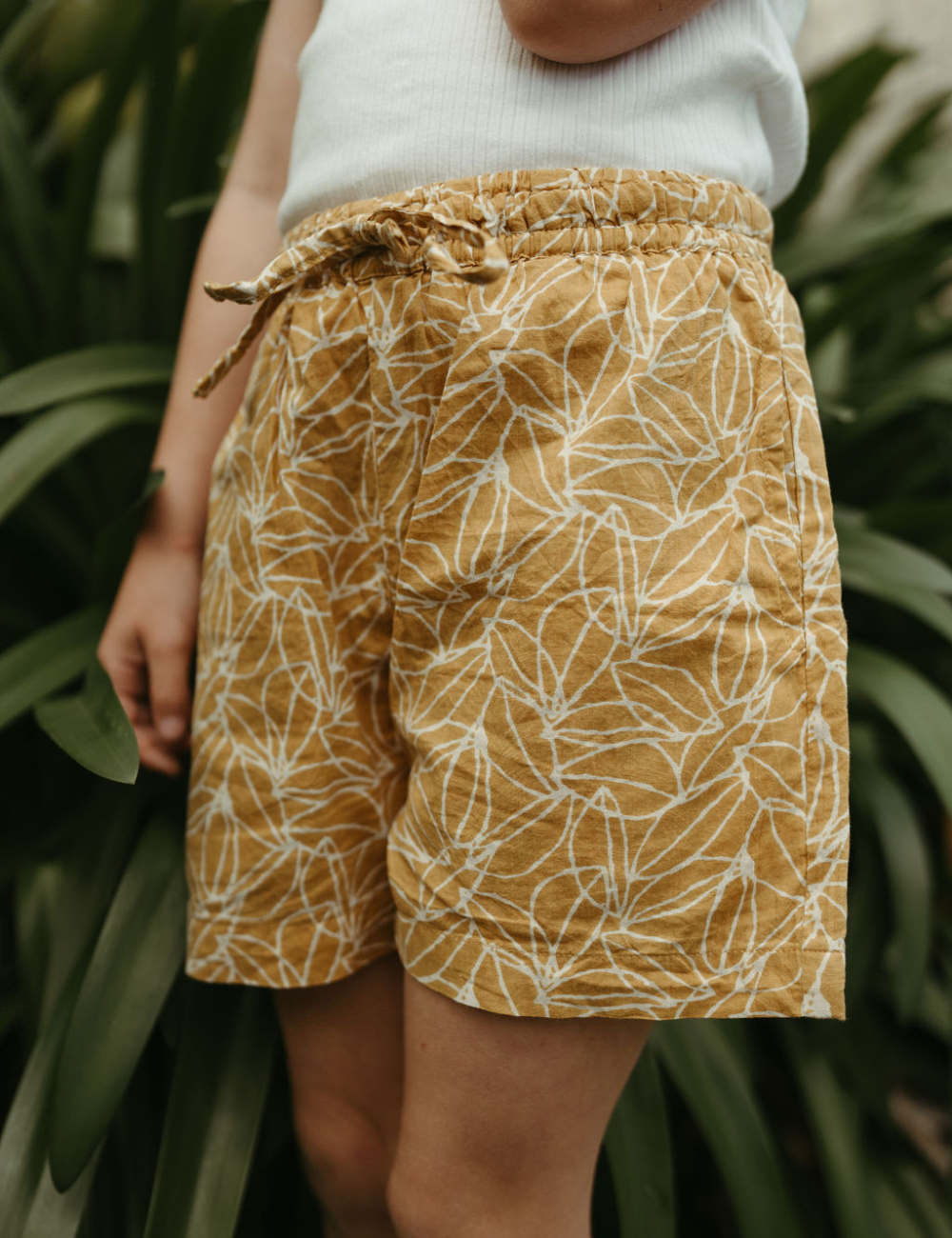 
                  
                    young girl wearing indian block printed shorts in mustard seed print in front of plant
                  
                