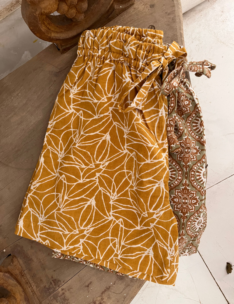 
                  
                    flat lay photo of indian block printed shorts in mustard seed and retro funk print on wooden shelf
                  
                