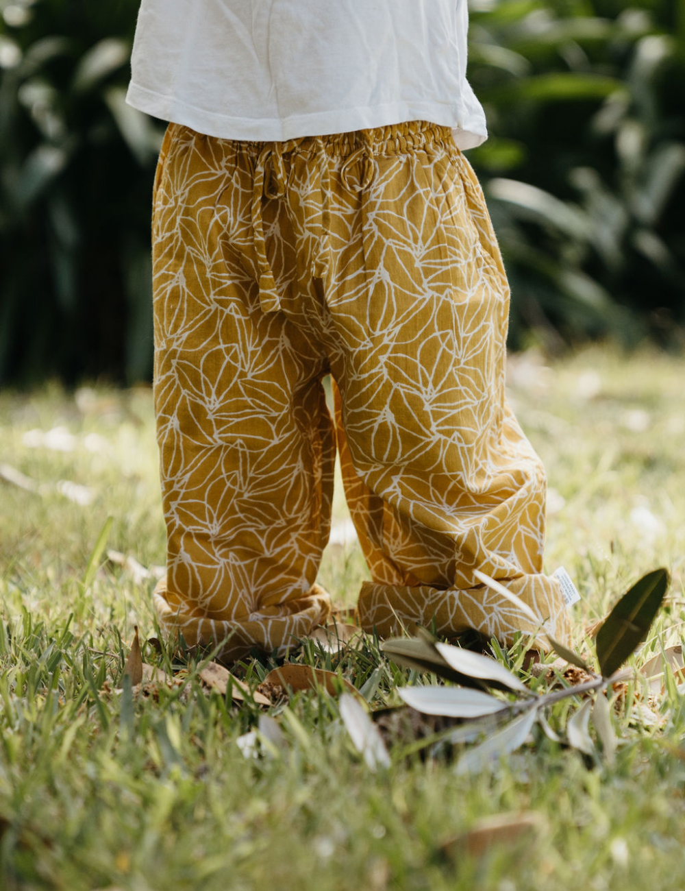 
                  
                    young child on lawn dressed in white singlet and Indian retro block printed pants in mustard seed print
                  
                