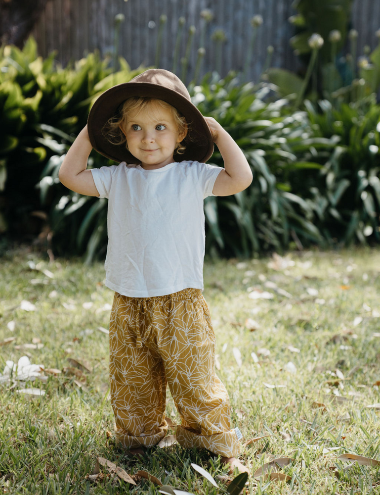 
                  
                    young child on lawn dressed in white singlet wearing a hat and Indian retro block printed pants in mustard seed print
                  
                