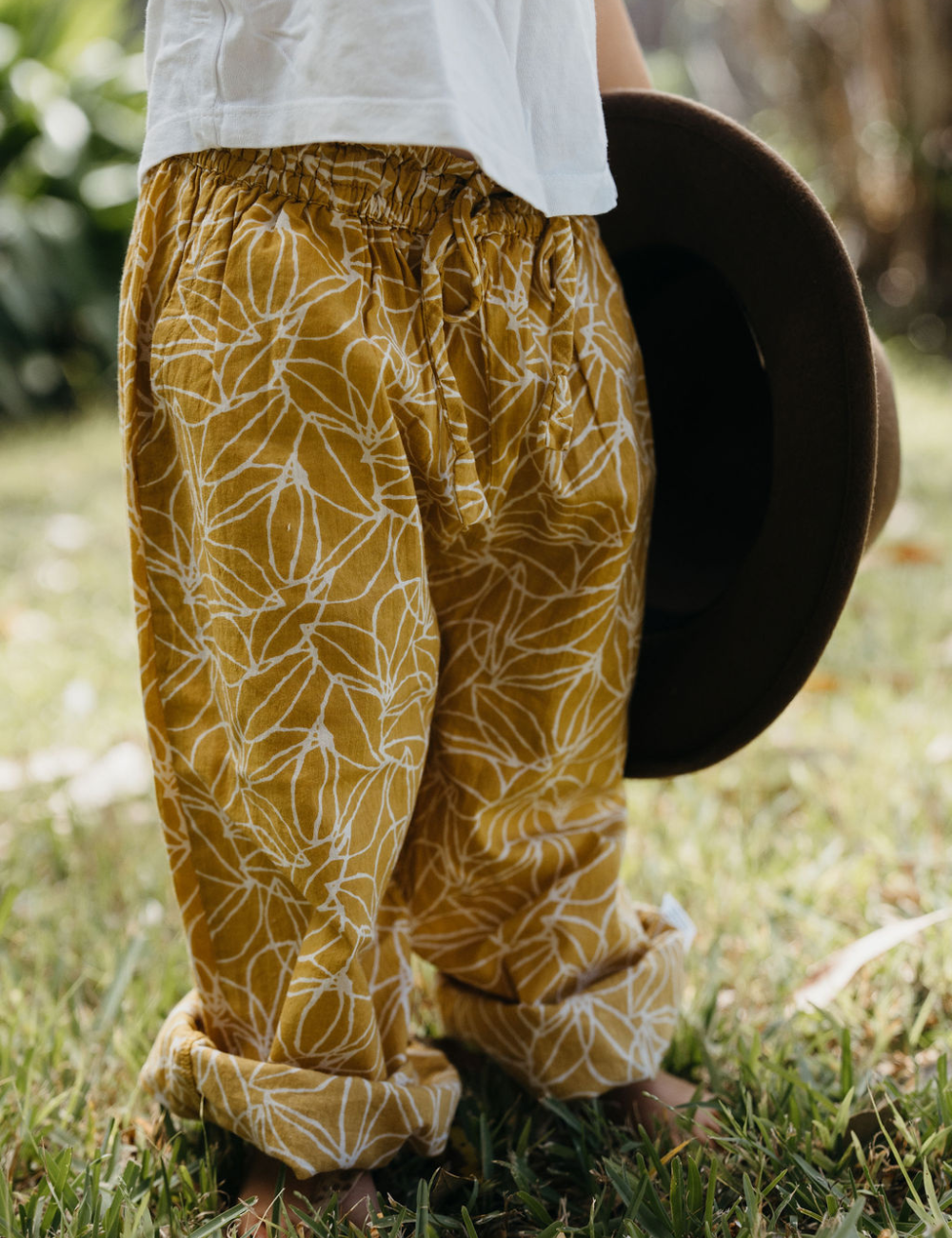 young child on lawn dressed in white singlet and Indian retro block printed pants in mustard seed print