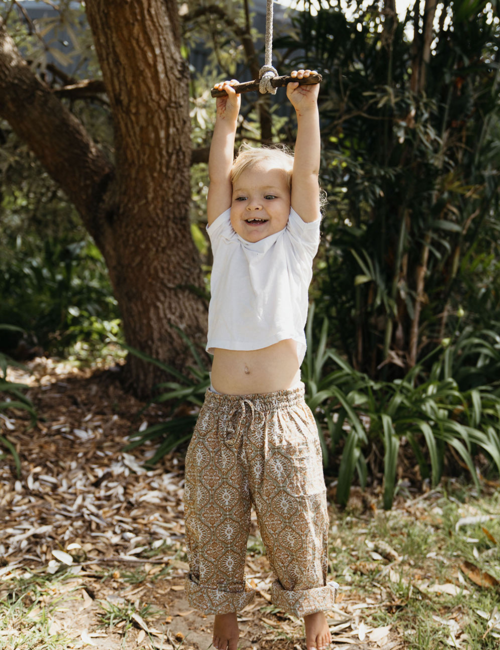 young girl swinging from a tree in forest dressed in white singlet and Indian retro block printed pants in retro funk print