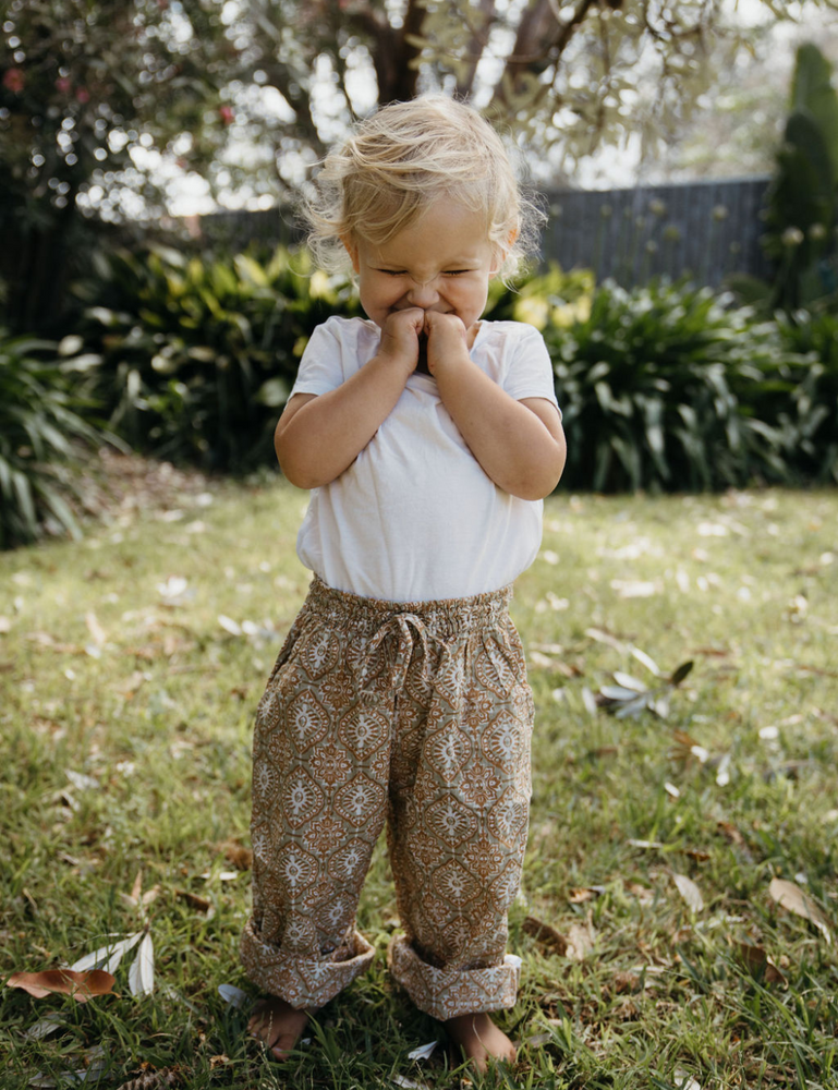 
                  
                    young girl giggling wearing white singlet indian block printed shorts in retro funk print on lawn
                  
                