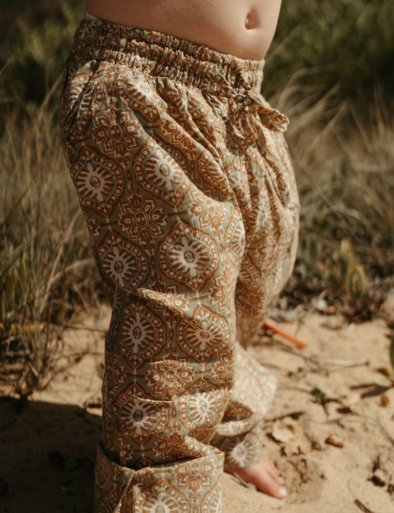 
                  
                    young child at the beach dressed in Indian retro block printed pants in retro funk print
                  
                