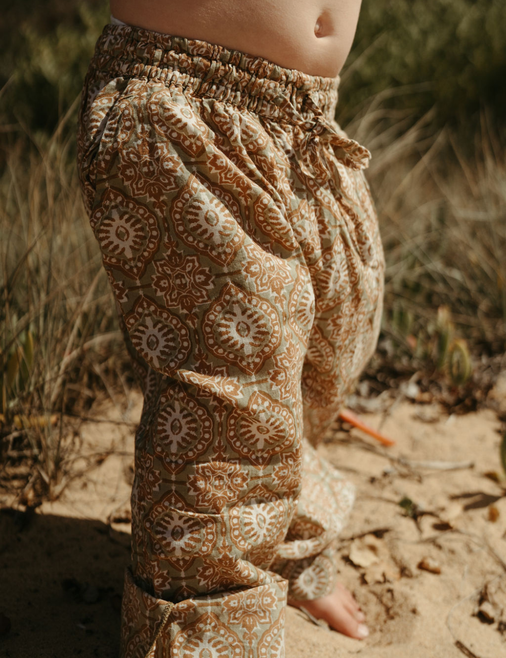 
                  
                    young child at the beach dressed in Indian retro block printed pants in retro funk print
                  
                