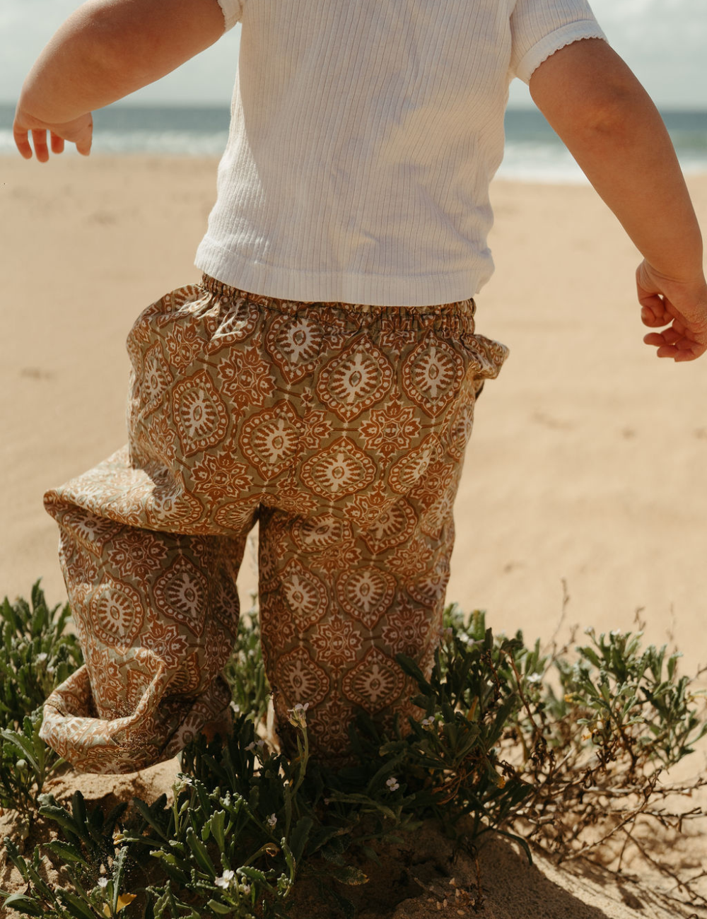 
                  
                    young child at the beach dressed in Indian retro block printed pants in retro funk print
                  
                