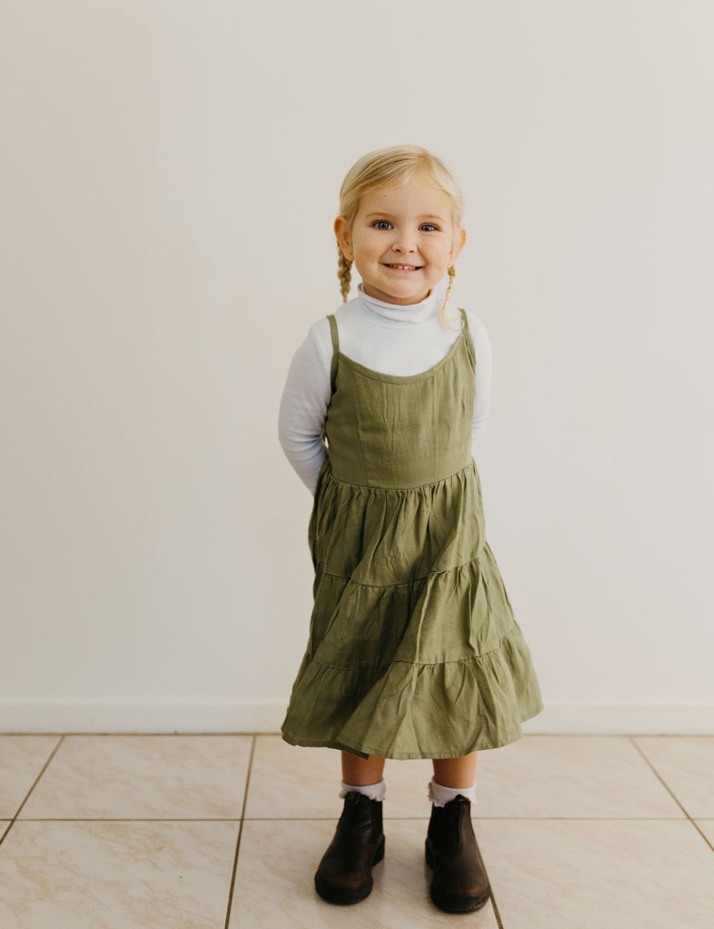 young girl dressed in vincente organic sugarcane tie dress in green forest standing in front of a white wall