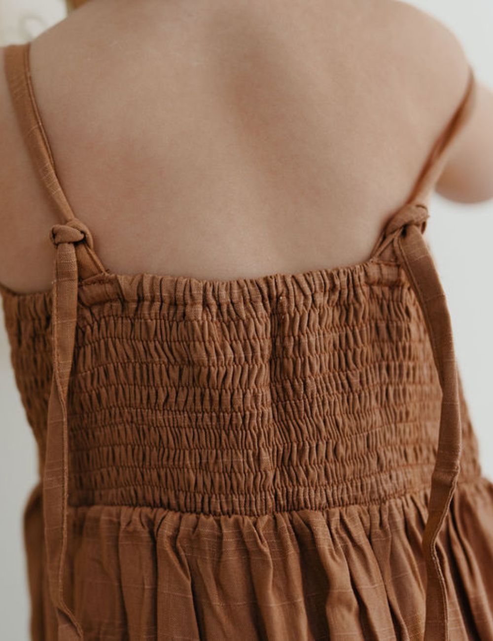 young girl dressed in vincente organic sugarcane tie dress in mulberry standing in front of a white wall