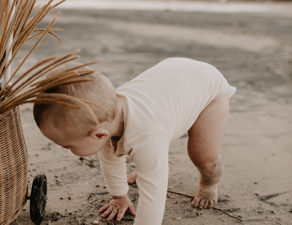 
                  
                    Young child in organic long sleeved romper in ribbed cream at beach in byron bay standing on all four
                  
                